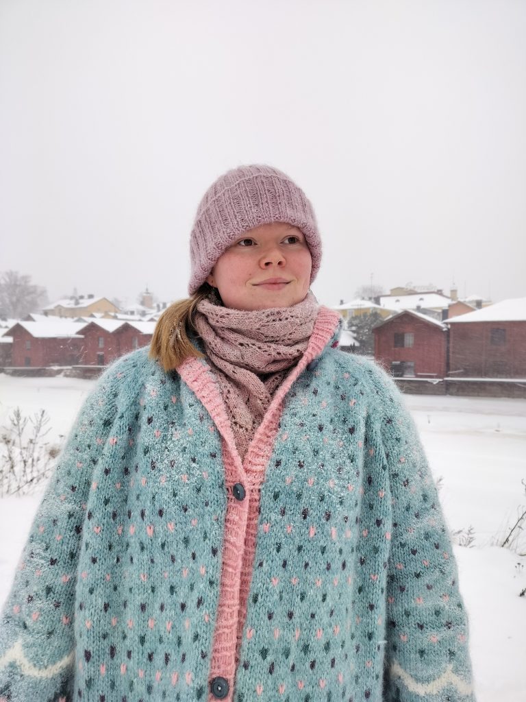 Vaaleanpunainen Halaus-pipo, pastellinen Kuura-takki, taustalla luminen Porvoo