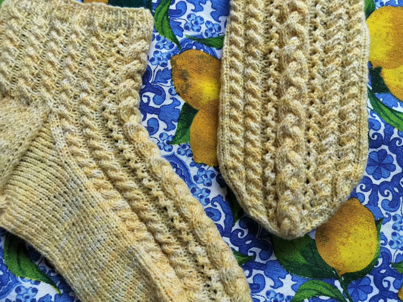 keltaiset villasukat, joissa on paljon ohuita palmikoita, kelta-sinisellä taustalla.