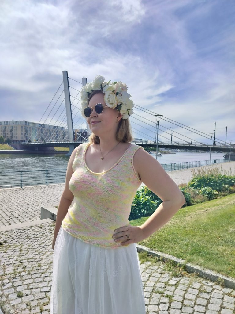 Pastellivärinen neuletoppi, valkoinen kukkaseppele, valkoinen pitsihame, kesäinen päivä