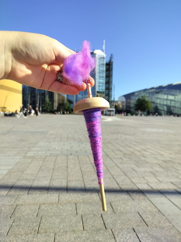 Puinen, yläpainoinen värttinä, jolla on pinkki-sinistä lankaa, Helsingin kansalaistorilla aurinkoisena päivänä.